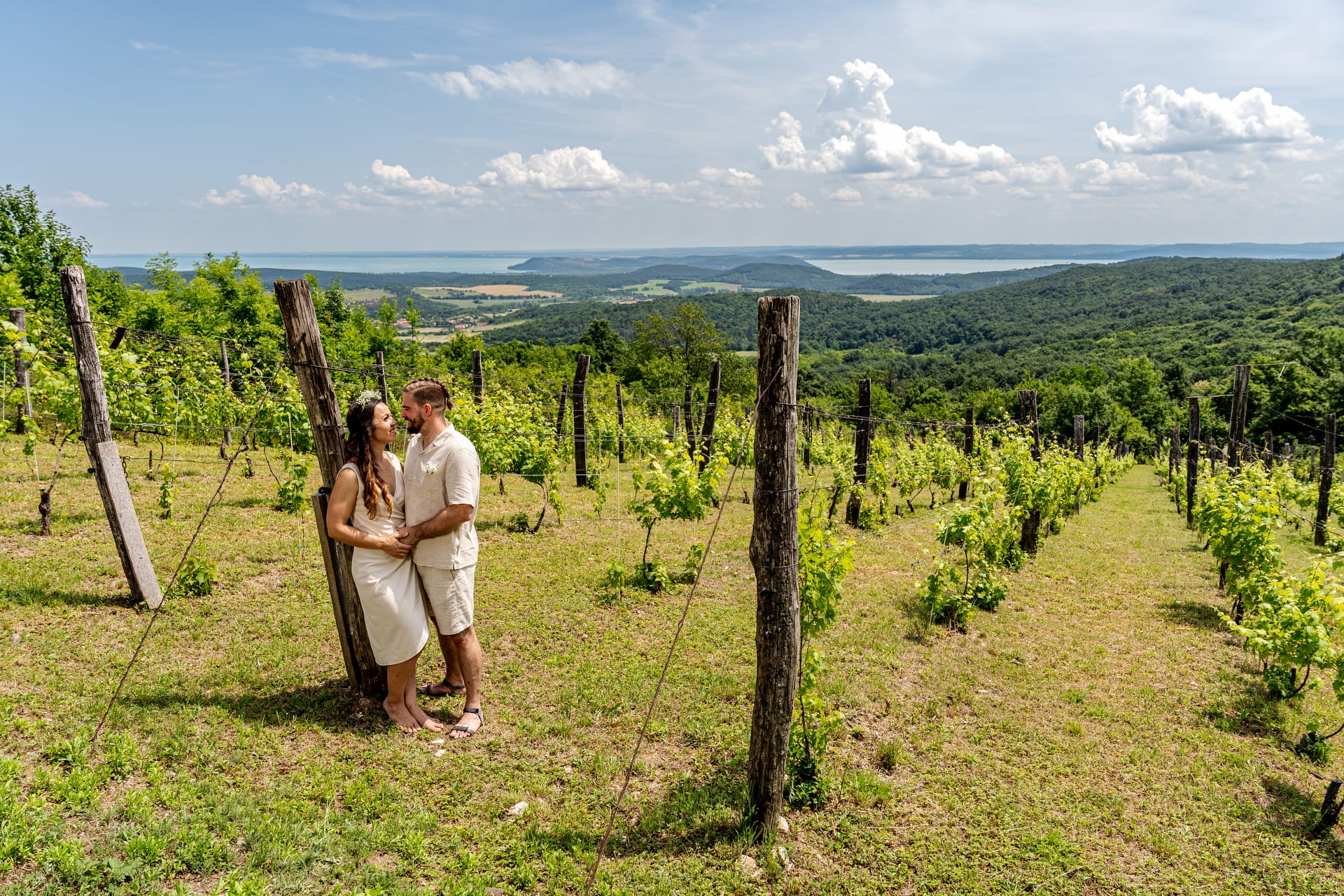 Friss házaspár kreatív fotózás közben a szőlősorok között a Balaton-felvidéken, háttérben a Balaton és a Tihanyi-félsziget.