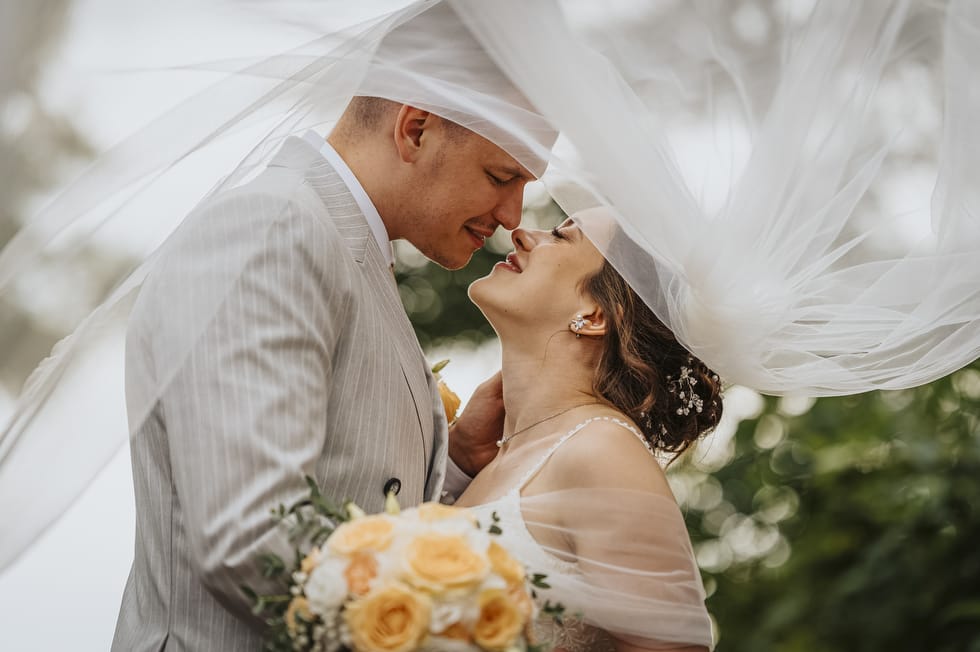 Friss házaspár az esküvői menyasszonyi fátyol alatt virágcsokorral