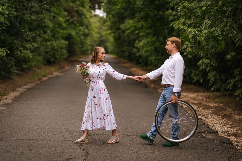 Jegyesfotózás közben sétál a fiatal pár a Hármashatár-hegyen, Budapesten kerékpárkerékkel a kézben.
