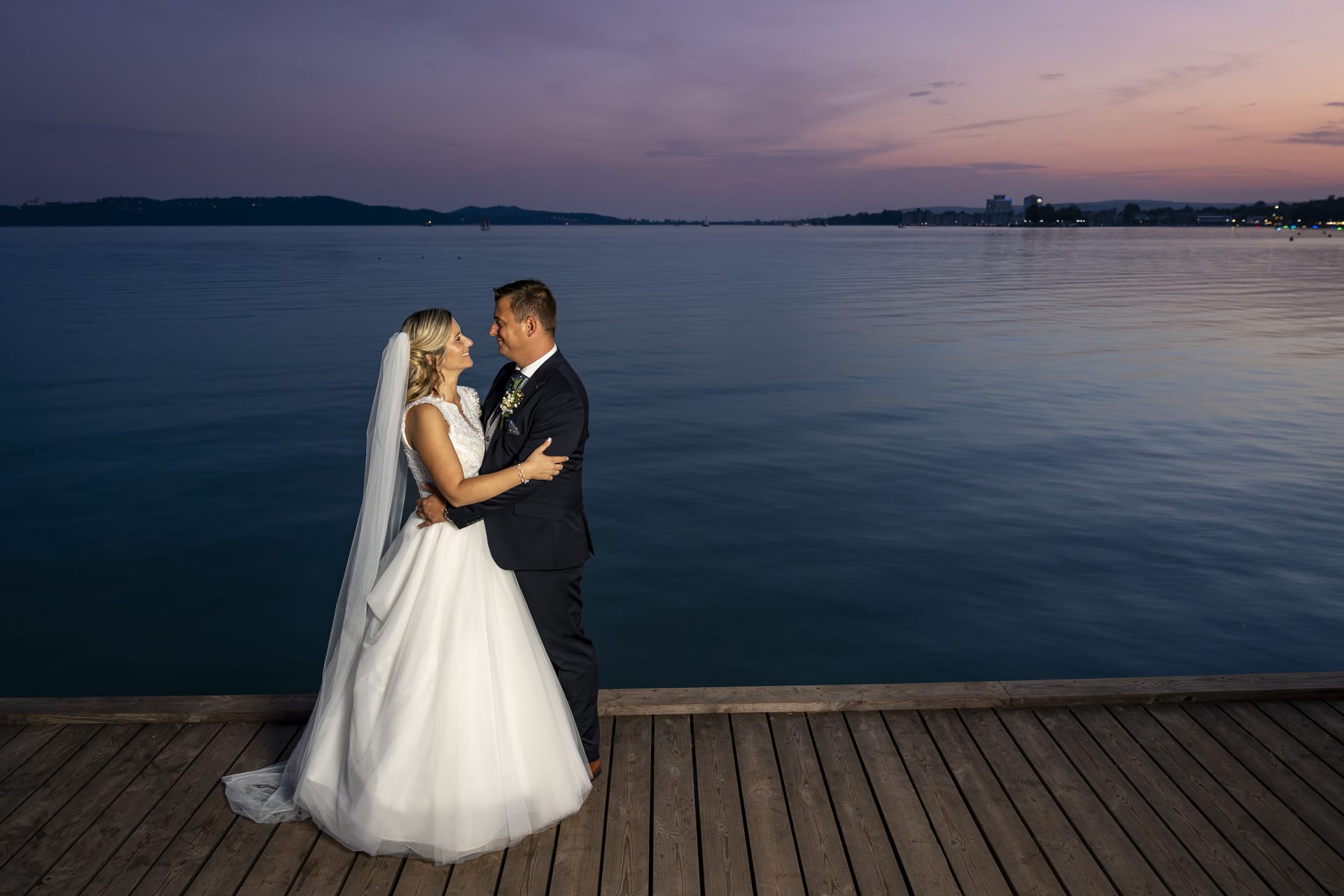 Vőlegény és menyasszony külön napi kreatív fotózáson naplemente idején egy stégen Balatonfüreden.