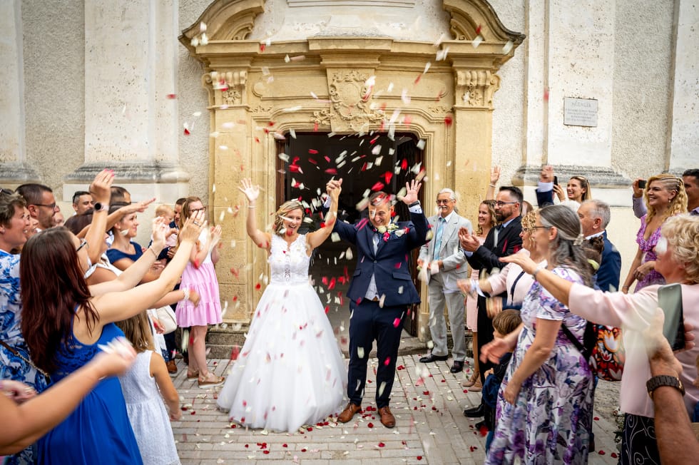 Friss házaspár kivonul a templomból a szertartás után, miközben a vendégek rózsaszirmot szórnak rájuk